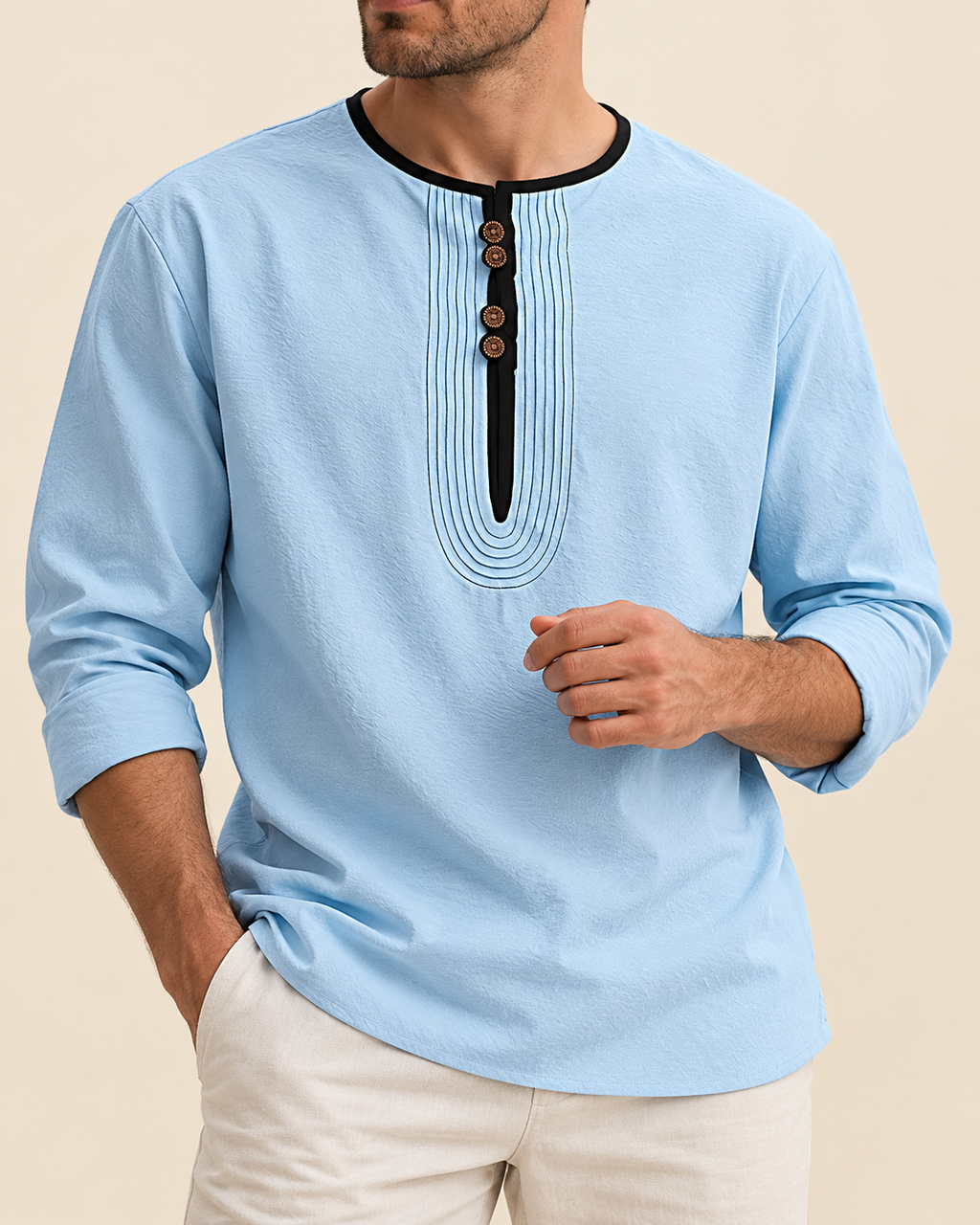 A man wearing a light blue long-sleeve kurta with a black contrast collar and a decorative black pleated placket with brown buttons, paired with off-white trousers, set against a solid beige background.