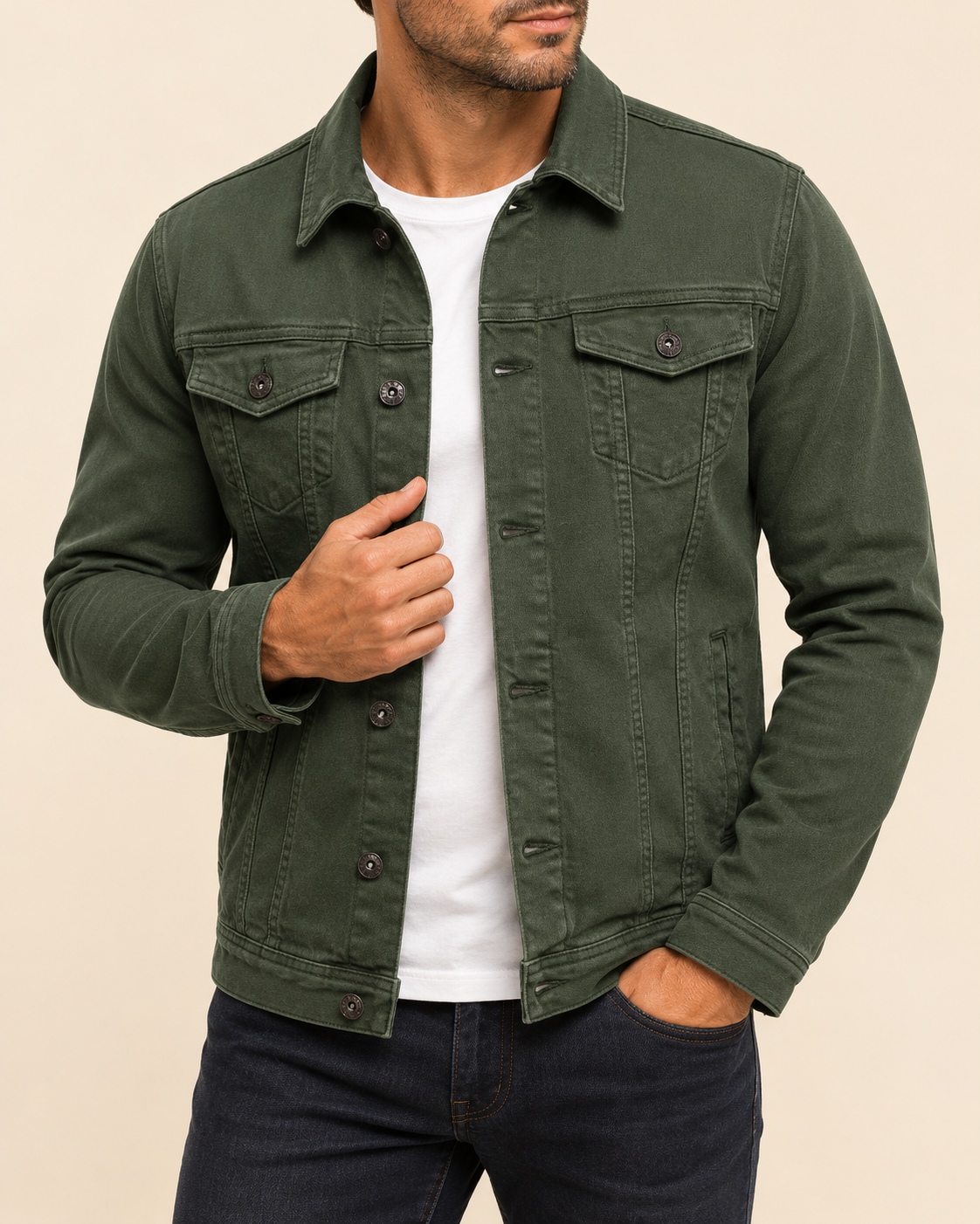 A man wearing an olive green button-up denim jacket over a white t-shirt and dark jeans, shown from the chin down against a solid beige background.
