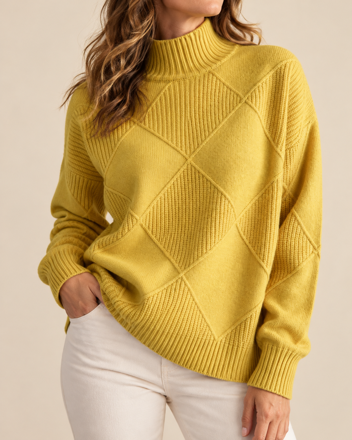 A woman wearing a mustard yellow ribbed knit mock neck sweater with a diamond argyle pattern on the front, paired with white pants, against a solid beige background.