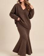 A woman wearing a brown fuzzy knit long-sleeve V-neck sweater dress with a flared mermaid-style hem, shown against a plain beige studio background.