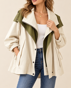 A woman wearing a cream and olive green color-blocked trench coat over a white tank top and blue jeans, photographed against a plain beige studio background.